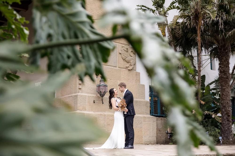 Bride and groom posing through greenery for romantic Santa Barbara Courthouse wedding photos.