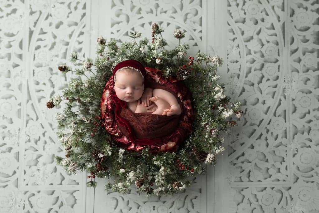 Christmas newborn photography with baby wrapped in festive blanket and fairy lights