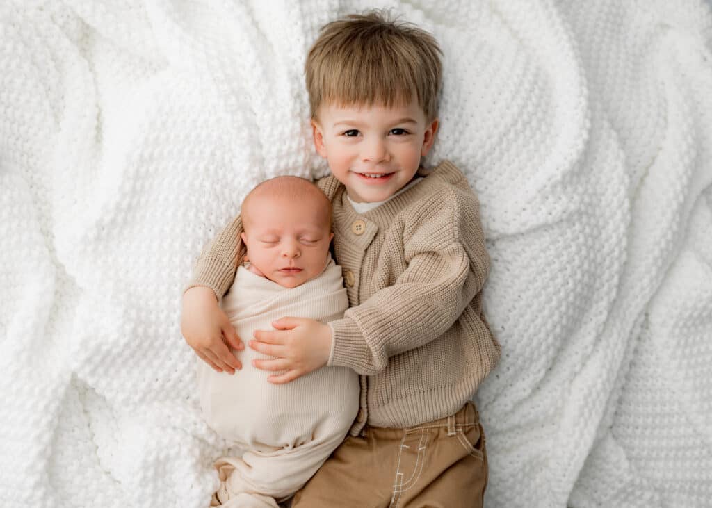 Older brother lying next to newborn baby, gently cuddling during a sibling photography session