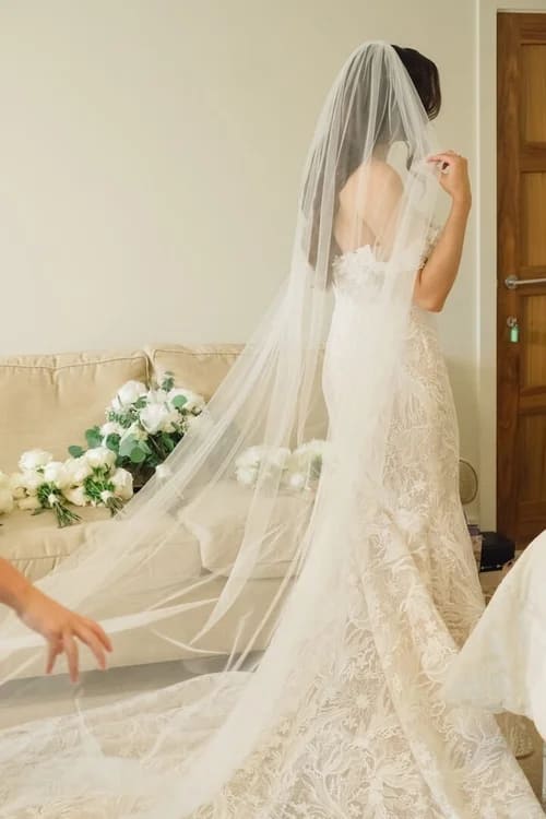 Bride adjusting her long lace veil during wedding photos bride getting ready moment.