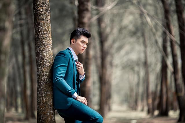 A stylish man standing near a tree in the forest showcasing natural light and outdoor fashion photo composition