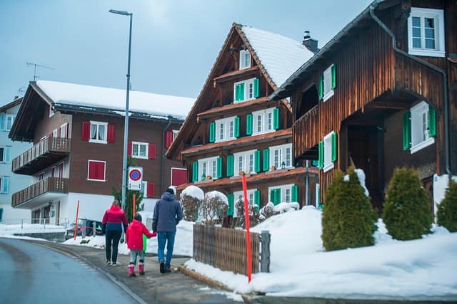 “A family walking together in the snow near houses, dressed in warm winter clothing, enjoying a snowy day outdoors.”