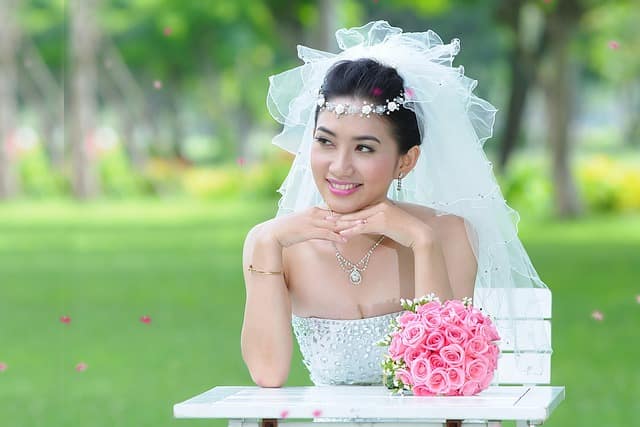 Beautiful bride sitting on lush green ground in her wedding dress, showcasing natural outdoor style from bridal photography packages.