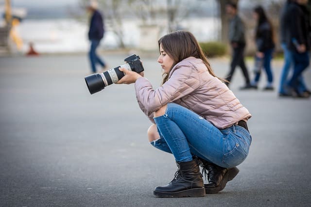 Photographer crouching outdoors with Canon camera and telephoto lens, illustrating Canon FL Service Manual use in field photography.