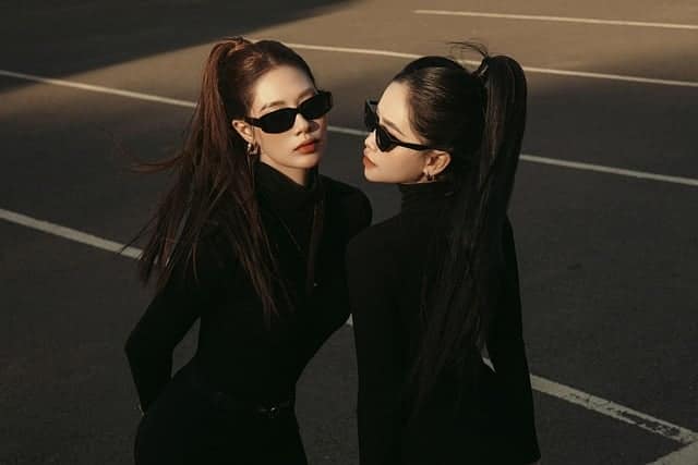 Two fashionable women posing in black outfits and sunglasses on a city street, perfect example for street style photo editing showcasing urban fashion tones and contrast.