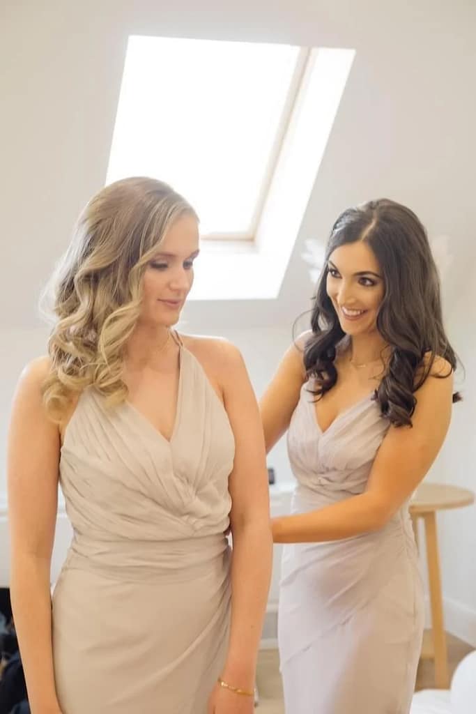 Bridesmaids helping each other get dressed during wedding photos bride getting ready.