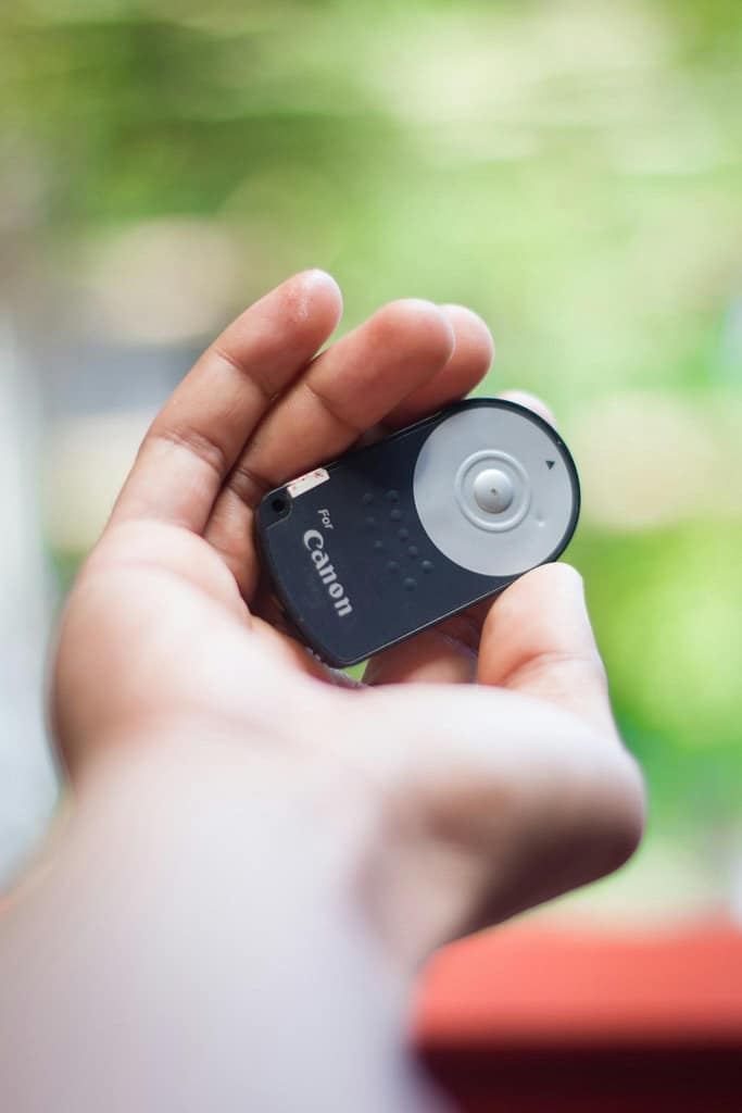 A person holding a Canon camera remote control — related to the topic Can You Use a Camera Solar Charger to Charge Battery showing camera accessories and power options.