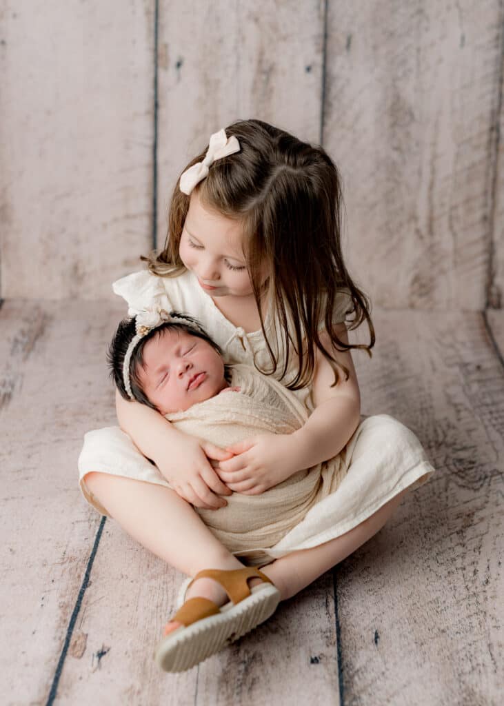 Older sibling gently holding newborn baby in cozy blanket during photography session
